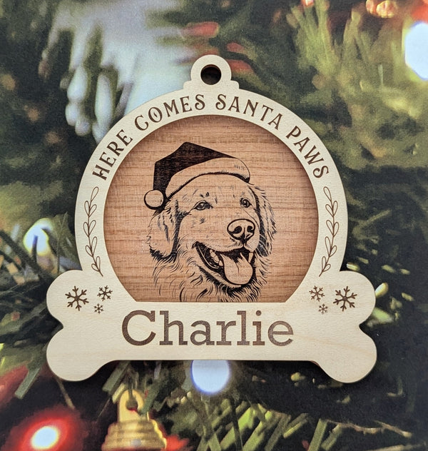 Wooden Christmas ornament with a dog illustration and text 'Here Comes Santa Paws Charlie' on a Christmas tree.